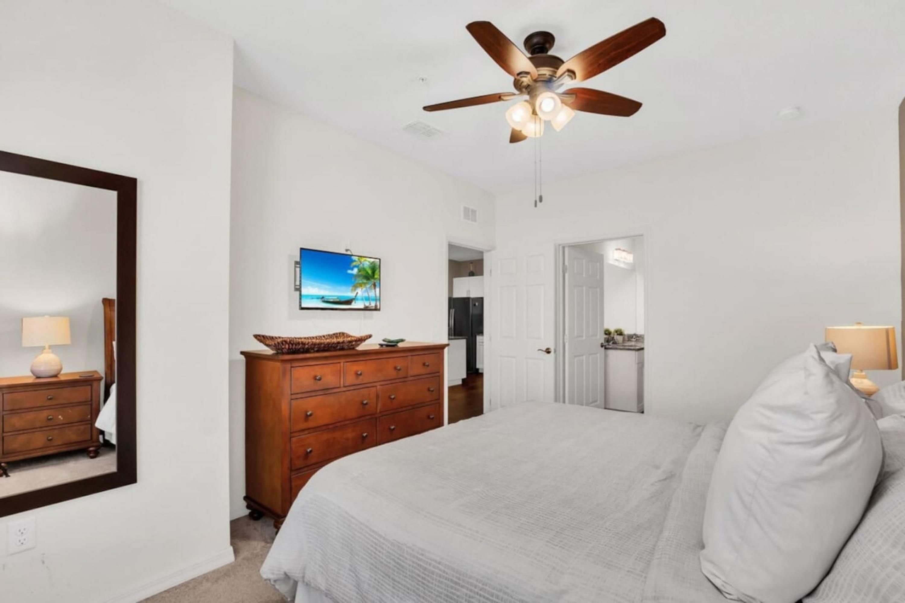 A bedroom with a bed, a ceiling fan, a dresser, a mirror, and a television.