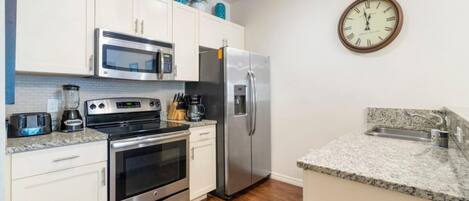 A modern kitchen with stainless steel appliances, white cabinets, and a granite countertop.