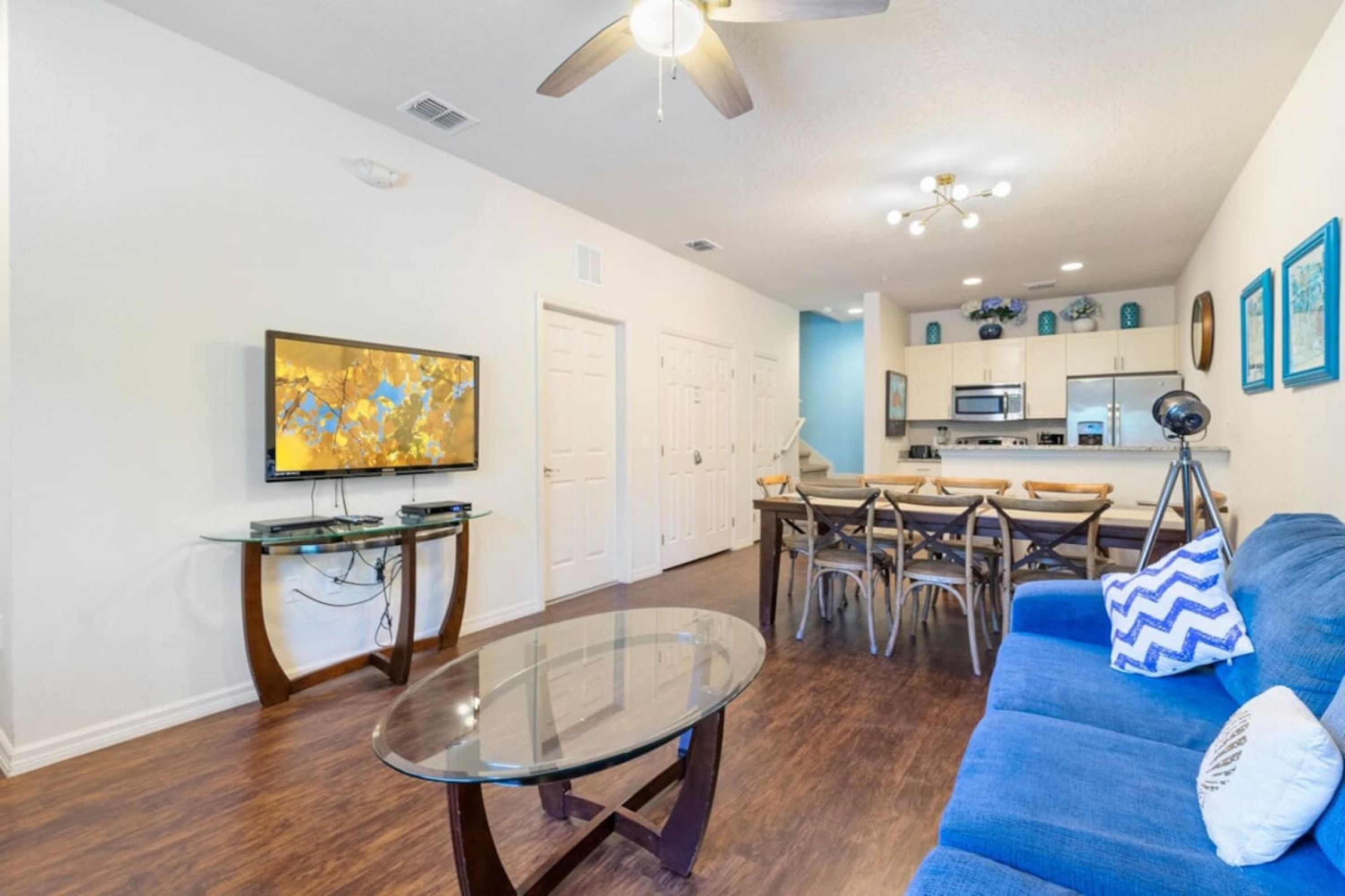 Un salon moderne avec une table basse en verre, un canapé bleu et un coin repas comprenant une table et des chaises blanches.