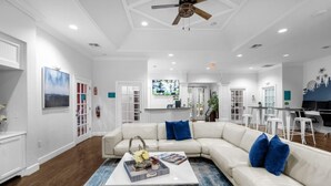Un salon spacieux avec un canapé d’angle blanc, une table basse agrémentée d’objets décoratifs et un ventilateur de plafond.