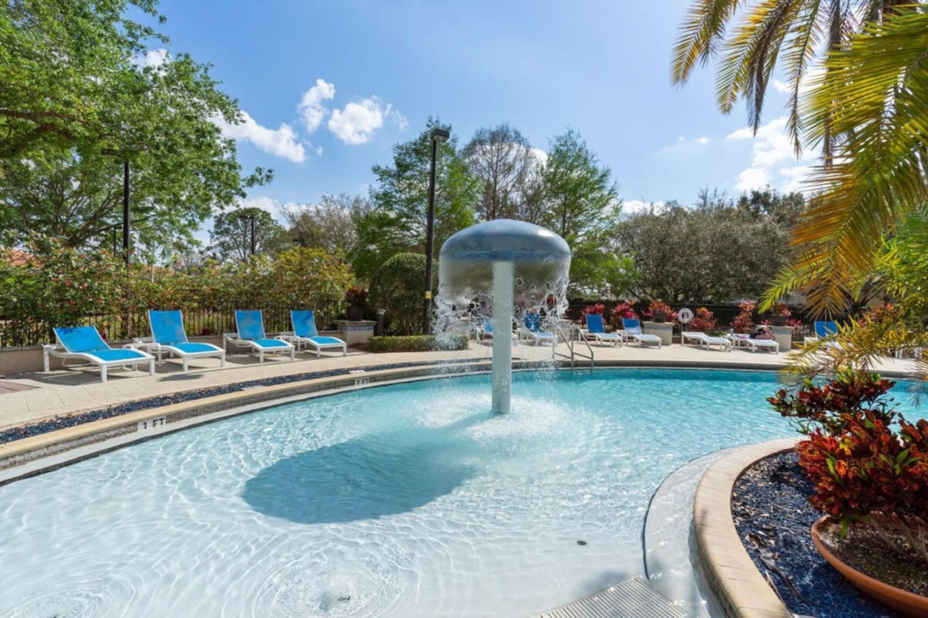 Une piscine agrémentée d’une fontaine, entourée de chaises longues et de palmiers.