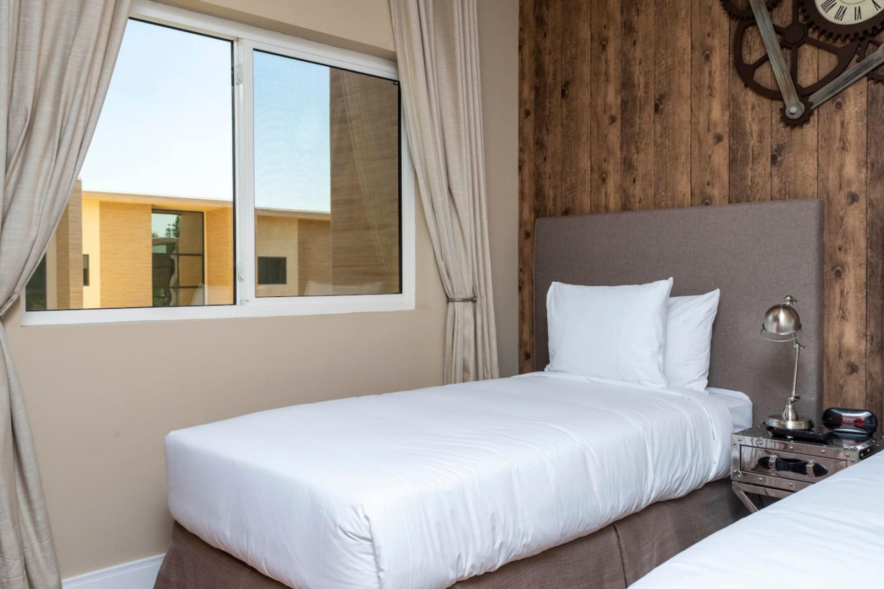 A hotel room with a bed, a nightstand, a clock, and a window with curtains.