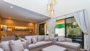 A modern living room with a sectional sofa, a coffee table, and a glass door leading to an outdoor area. - Luxury 3bdr House Near Disney 7527 (Kissimmee)