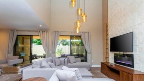 A modern living room with a sectional sofa, a flat-screen TV mounted on a brick wall, and a glass door leading to an outdoor area. - Luxury 3bdr House Near Disney 7527 (Kissimmee)