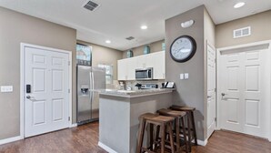 A kitchen with a central island, bar stools, a microwave, and a refrigerator.