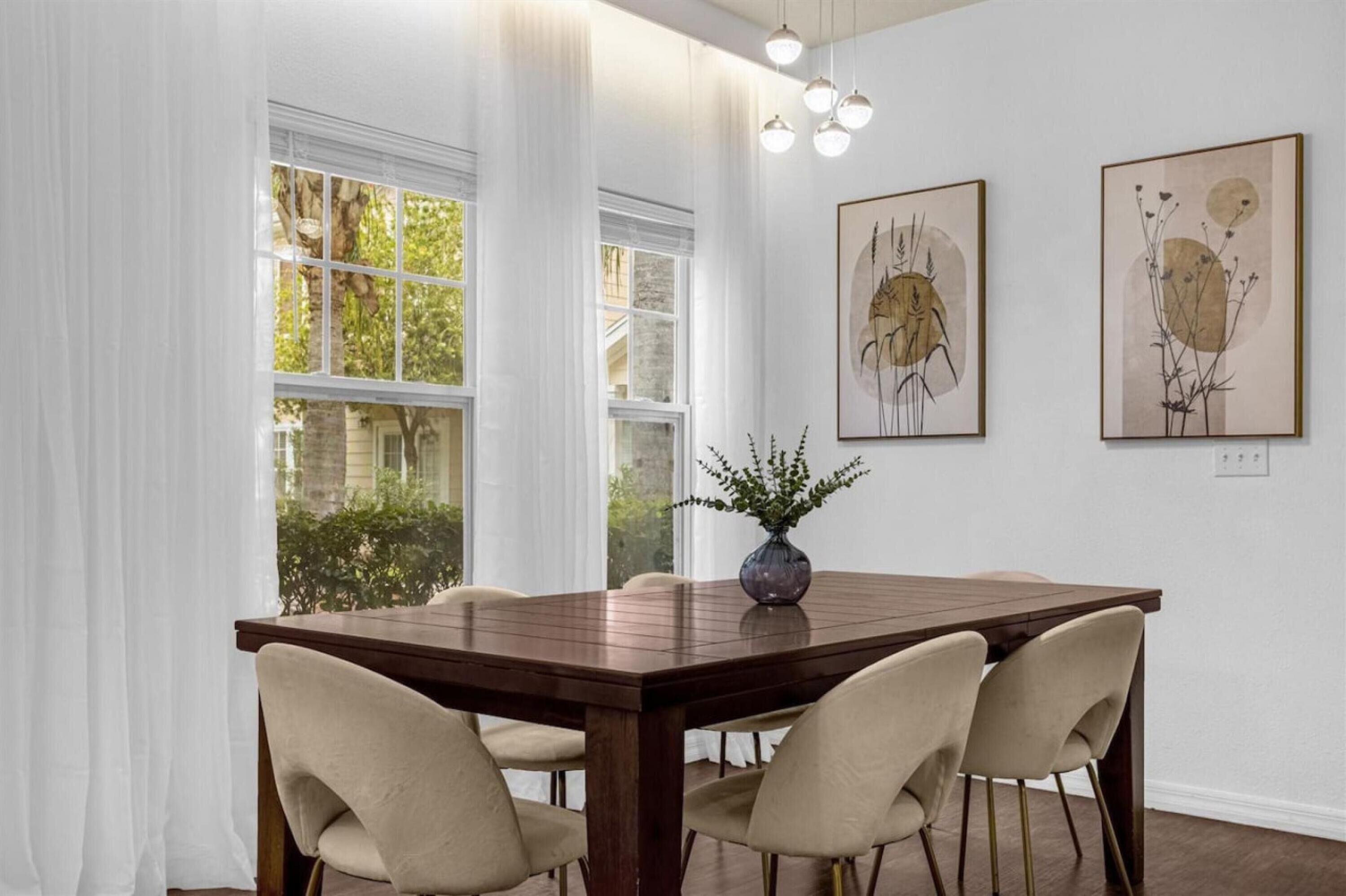 Een eetgedeelte met een houten tafel, beige stoelen en twee kunstwerken aan de muur.