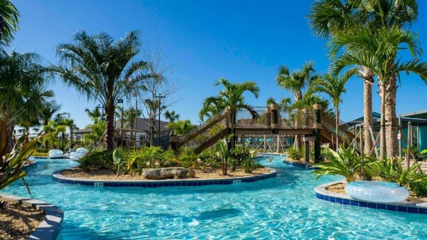 A swimming pool area with palm trees, a slide, and a small bridge. - Amazing 5bdr Disney Vacation With Pool - 4365 (Kissimmee)