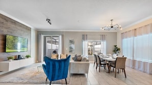 A modern living room with a TV, blue chair, sofa, dining table, and chairs. - Amazing 5bdr Disney Vacation With Pool - 4365 (Kissimmee)
