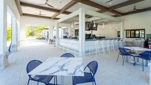 A spacious outdoor dining area with white tables and blue chairs, a bar area with white stools, and ceiling fans. - Amazing 5bdr Disney Vacation With Pool - 4365 (Kissimmee)