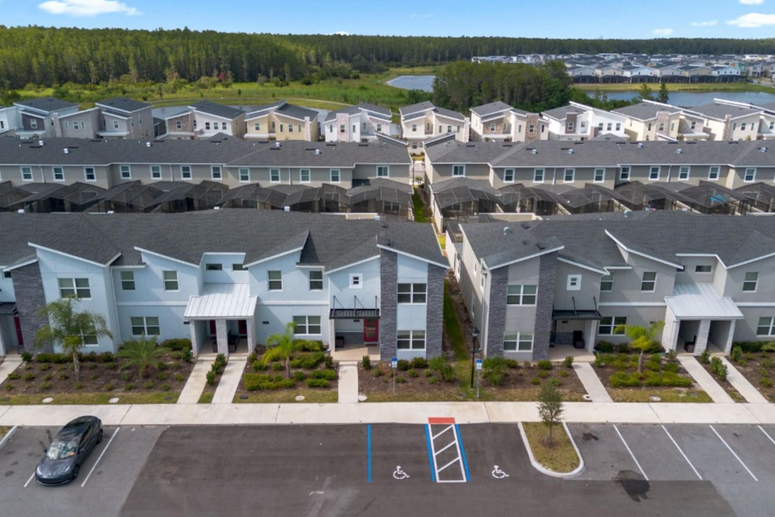 A residential complex with multiple townhouses, a parking area, and a small body of water in the background.