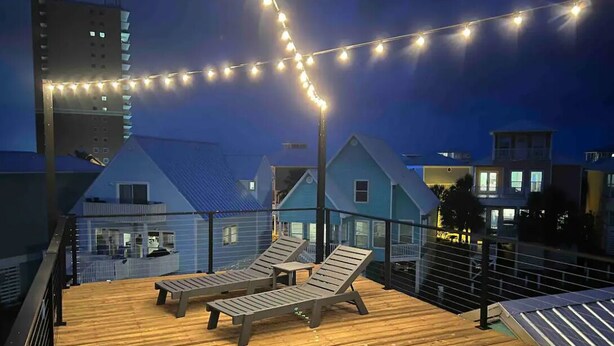 Una terraza de madera con dos sillones reclinables y luces colgantes.