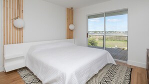 Un dormitorio con una cama grande, un cabecero de listones de madera, un ventanal con vistas al exterior y una lámpara en el techo.