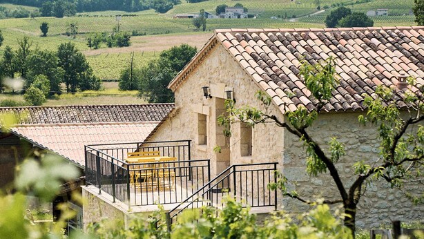 A stone building with a tiled roof, a balcony with a black railing, and a vineyard in the foreground. - Gîte au Cœur des Vignes (Montagne)