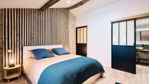 A bedroom with a large bed, wooden slats on the wall, a stone accent wall, and a sliding door to the right. - Gîte au Cœur des Vignes (Montagne)