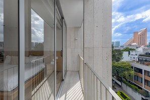 A balcony with a bed, a glass door, and a city view.