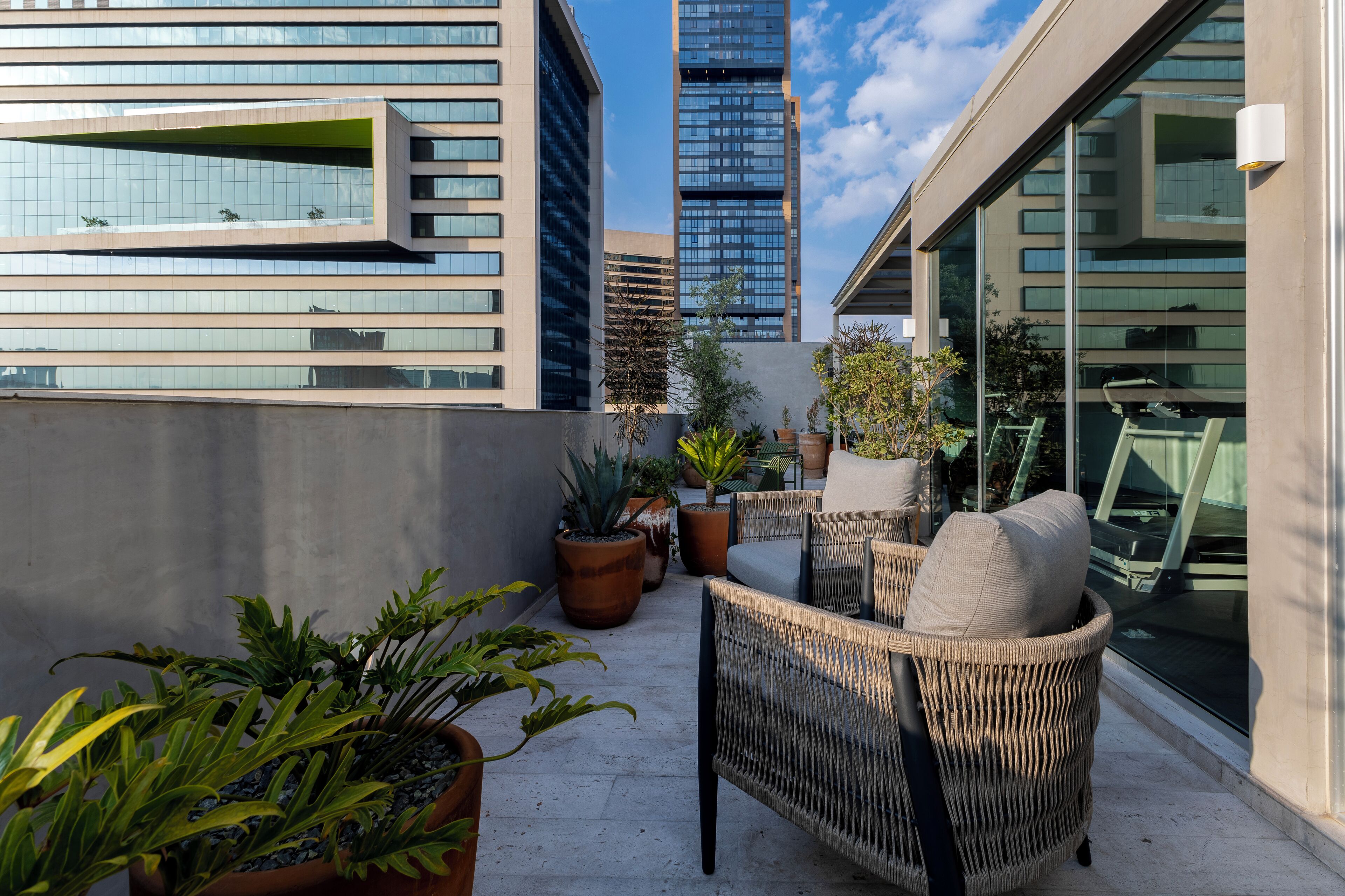 A rooftop terrace with wicker furniture, potted plants, and a view of modern buildings.