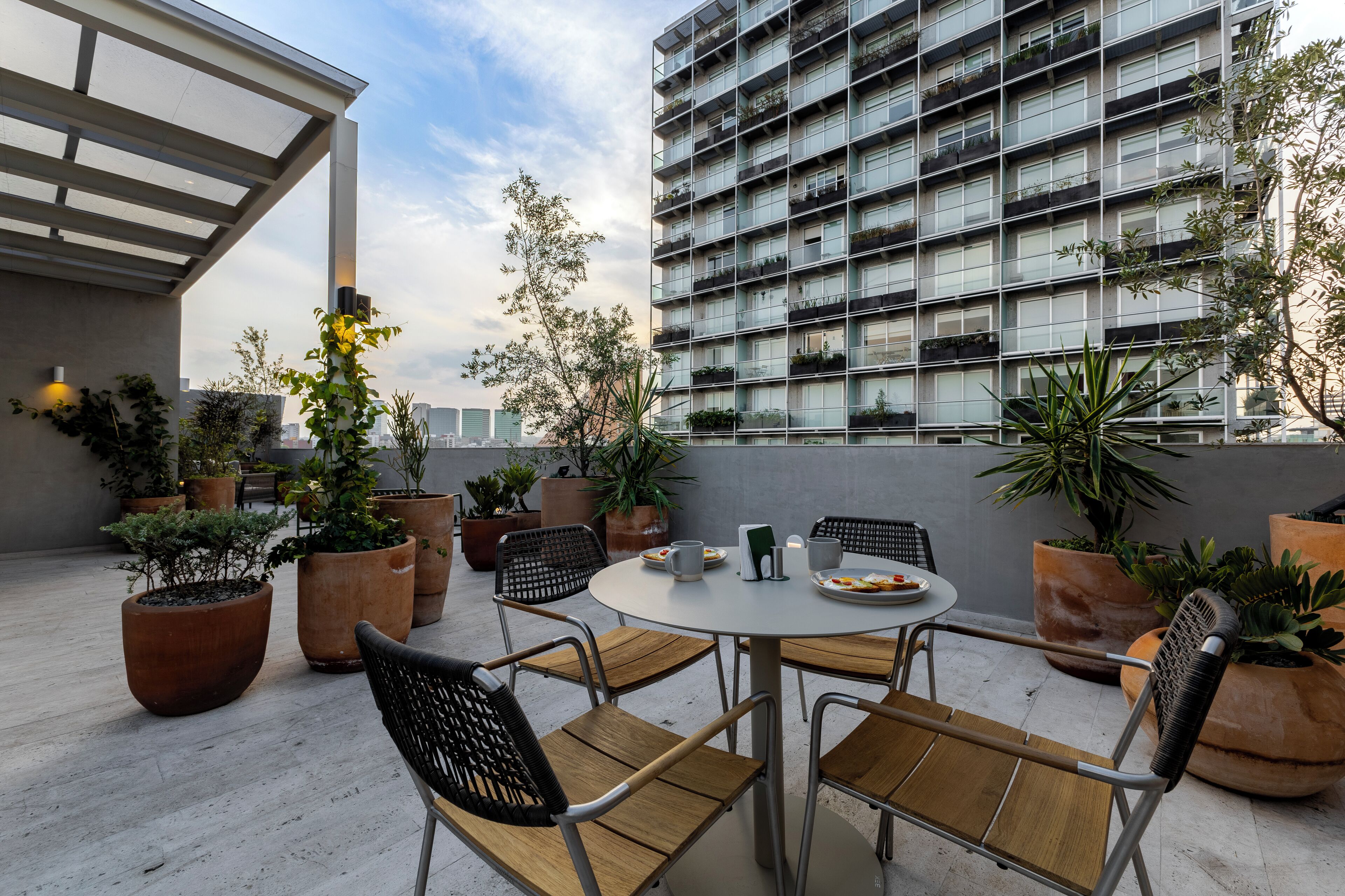 Une terrasse sur le toit, avec une table ronde, des chaises et des plantes en pot.