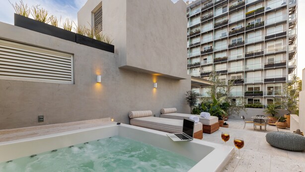A modern outdoor relaxation area with a hot tub, seating, and a view of a high-rise building.