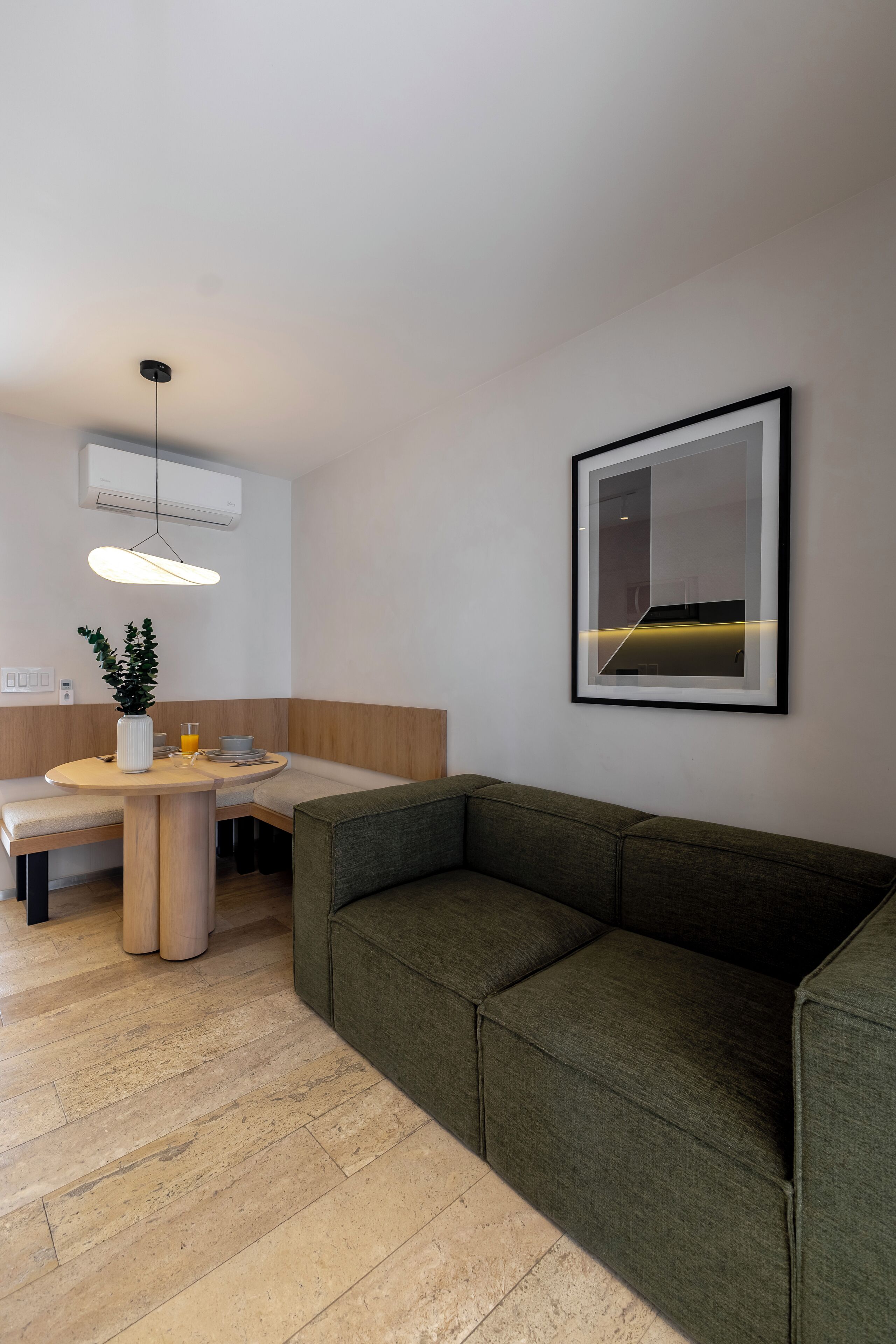 Ein modernes Wohnzimmer mit einem grünen Sofa, einem Esstisch mit einer Vase und einem Glas sowie einem gerahmten Kunstwerk an der Wand.