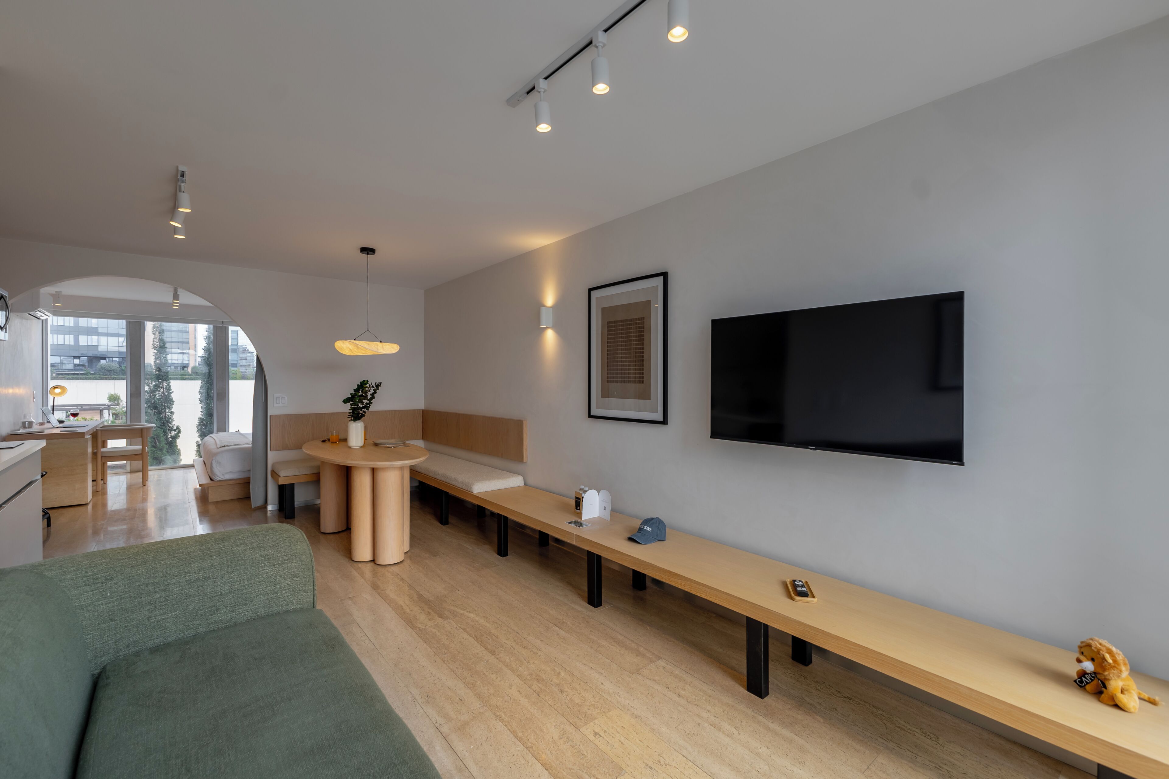 Uma sala de estar moderna com um sofá, um banco de madeira comprido, uma TV fixada na parede e uma pequena mesa com uma planta.