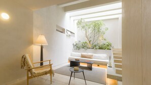 A modern living room with a sofa, a chair, a coffee table, a lamp, and a view of a tree through a window.
