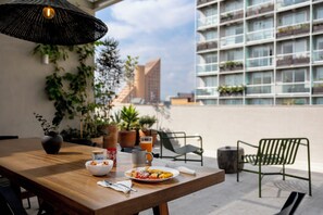 A dining table with a meal, a drink, and a basket of bread. There are potted plants and a chair in the background.