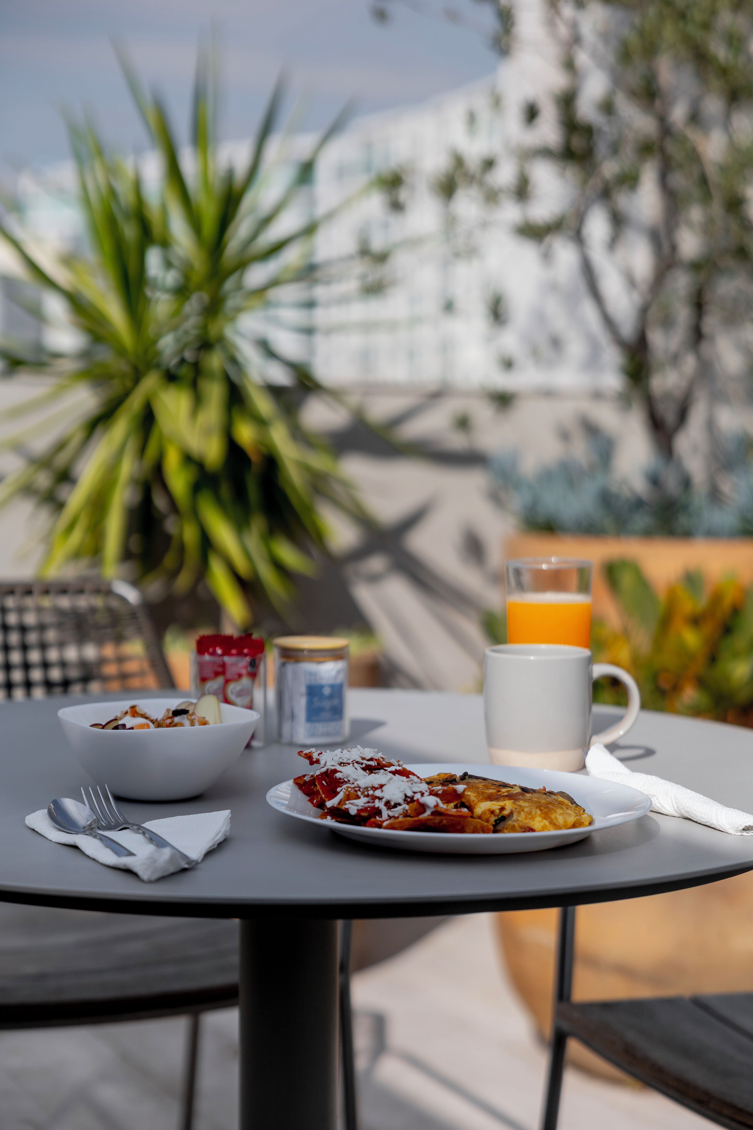 Une table avec des aliments pour le petit-déjeuner, notamment un bol, une assiette avec de la nourriture, un verre de jus d’orange et une tasse.