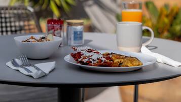 Una mesa con alimentos para el desayuno, incluyendo un bol, un plato con comida, un vaso de jugo de naranja y una taza.