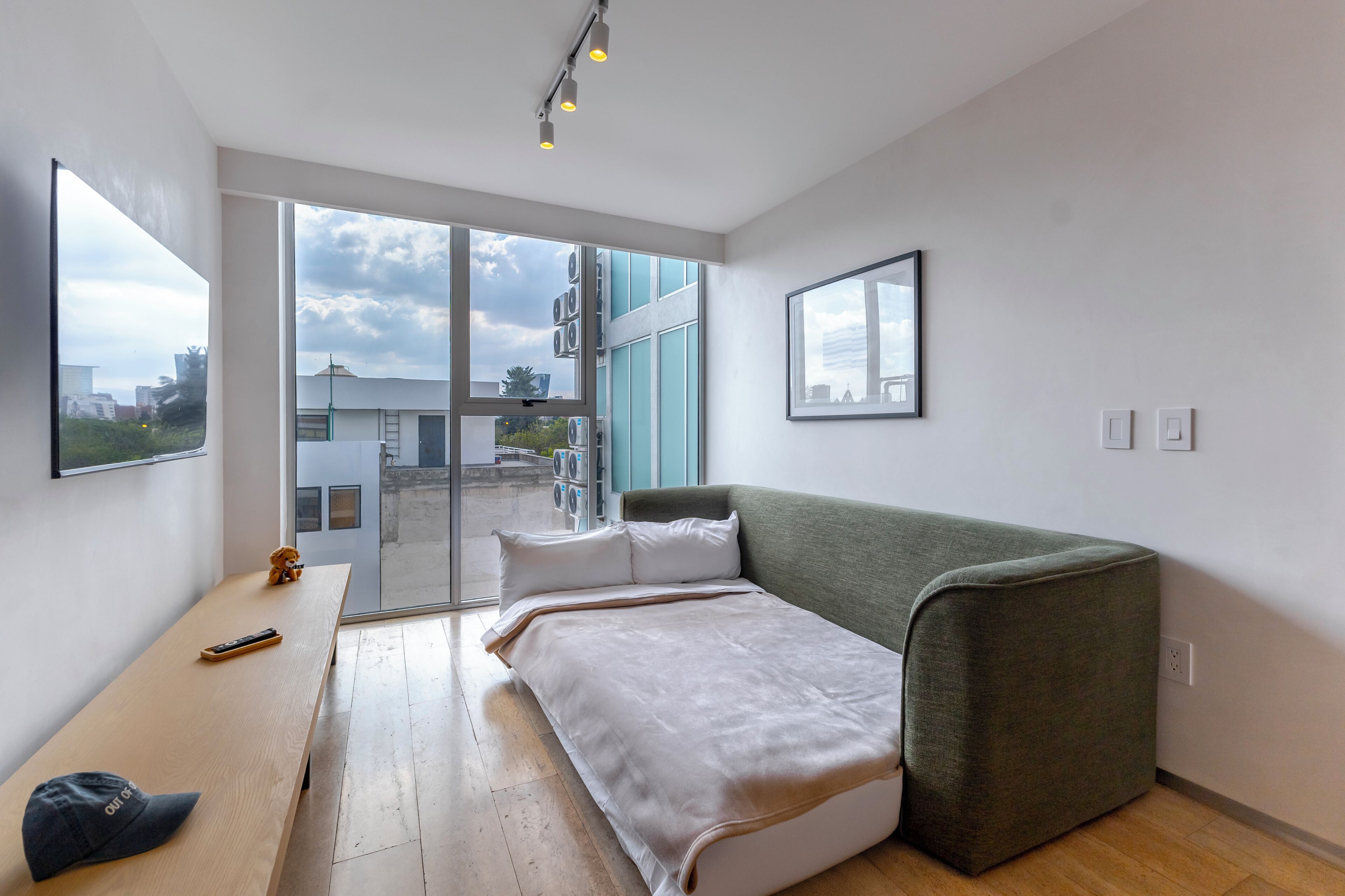 A modern room with a bed, a bench, a small table, and a large window.