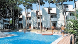 A swimming pool surrounded by trees and a white building with balconies.