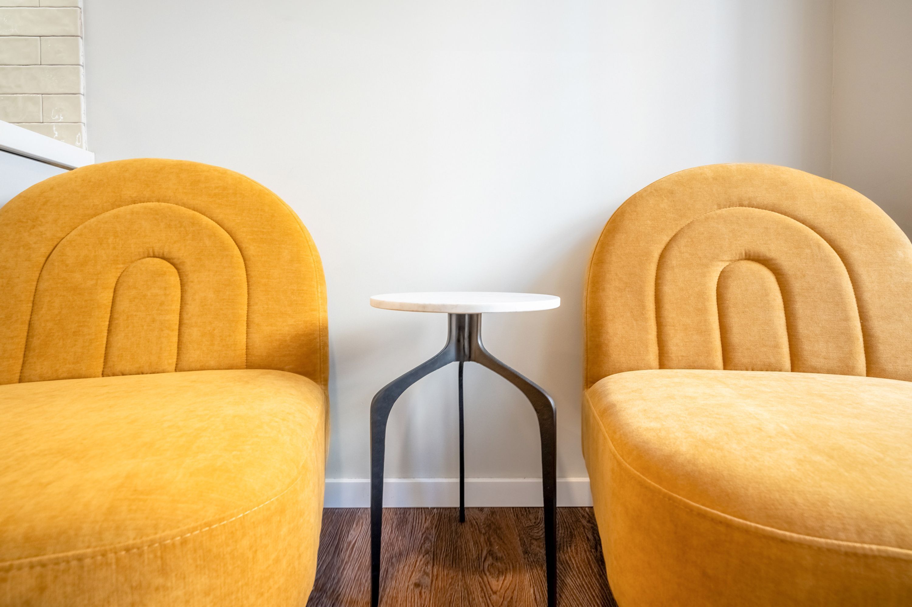 Deux fauteuils jaunes et une petite table ronde se trouvent dans une pièce dont le mur est blanc et le sol est en bois.