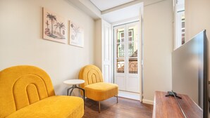 A room with two yellow armchairs, a small round table, and a TV on a wooden stand. - Bairro Alto Prime Studio I by Homing (Lisbon)