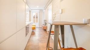 A narrow hallway with a wooden floor, a small table with a chair, and a door leading to another room. - Bairro Alto Prime Studio I by Homing (Lisbon)