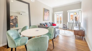 A modern living room with a round table, two green armchairs, a grey sofa with red cushions, and a large mirror. - Bairro Alto Prime Duplex by Homing (Lisbon)