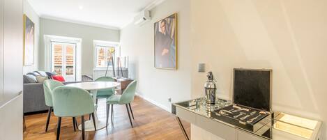 A modern kitchen with a dining area, wooden flooring, and a glass cabinet with kitchen tools.