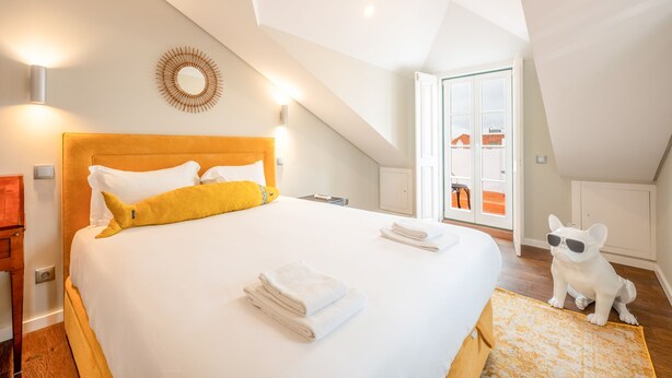 A hotel room with a large bed, a wooden headboard, and a view of the outside through a glass door. - Bairro Alto Prime Duplex by Homing (Lisbon)