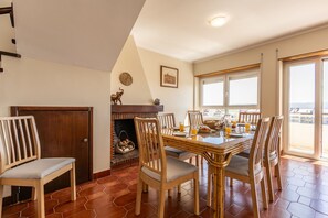 Un espace repas comprenant une table en bois, des chaises, une cheminée et une vue dégagée grâce à de grandes fenêtres.