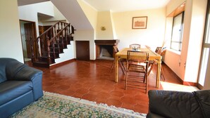 Una sala de estar con una escalera de madera, una mesa de comedor con sillas y un tapete estampado.