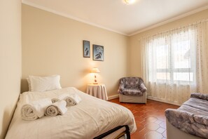 A hotel room with a bed, a chair, a table, and a window with curtains. - Bella Vista - Junto Praia (Alcobaça)