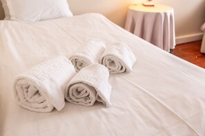 A neatly made bed with rolled white towels and a small round table with a lamp. - Bella Vista - Junto Praia (Alcobaça)