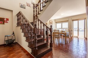 A staircase with wooden balusters leading to a dining area with hexagonal tiles and a view through glass doors. - Bella Vista - Junto Praia (Alcobaça)
