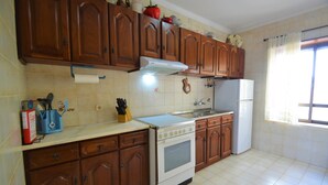Una cocina con armarios de madera, estufa, refrigerador y una ventana con cortinas.