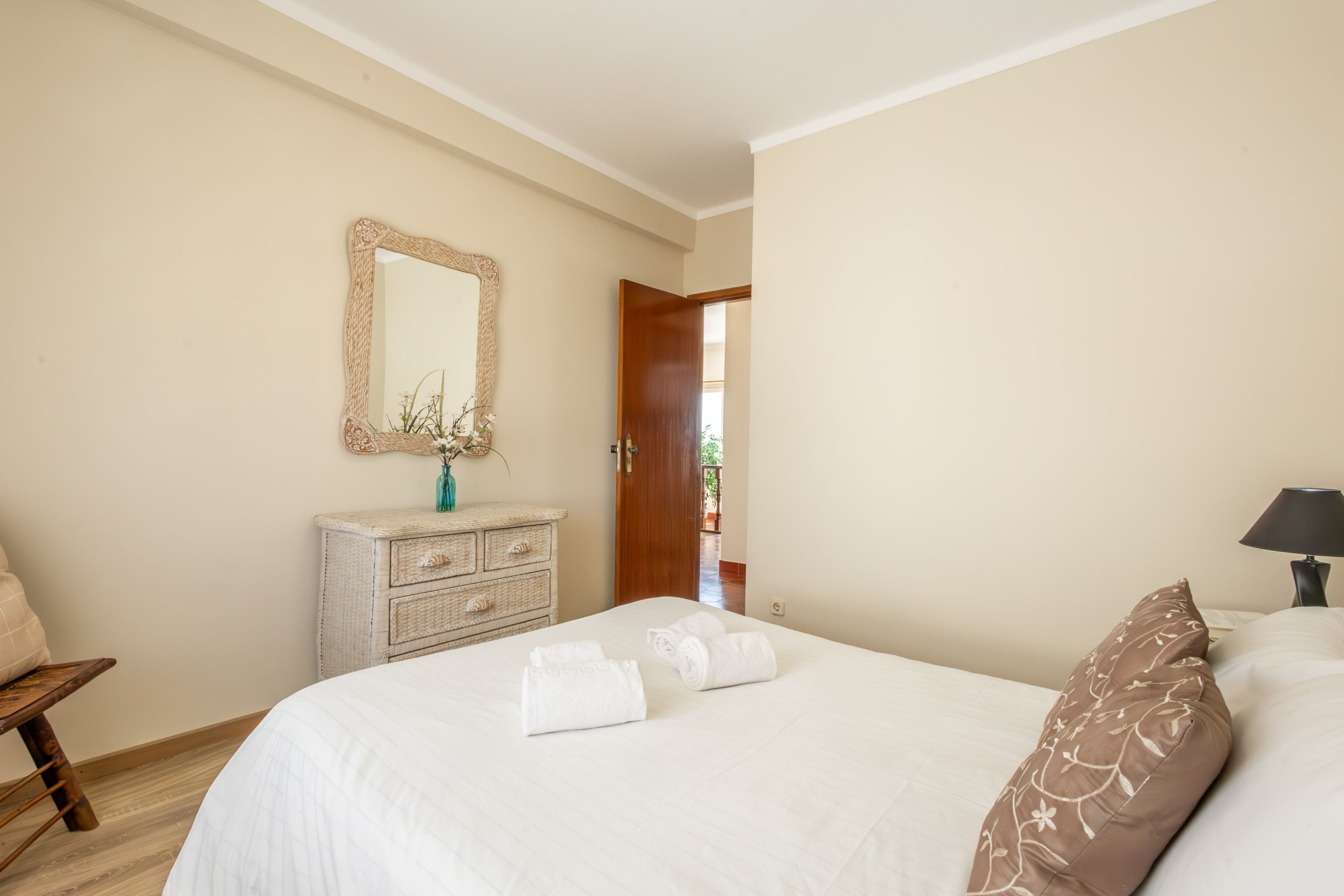 Um quarto com cama, cômoda, espelho e porta que dá para uma área externa.