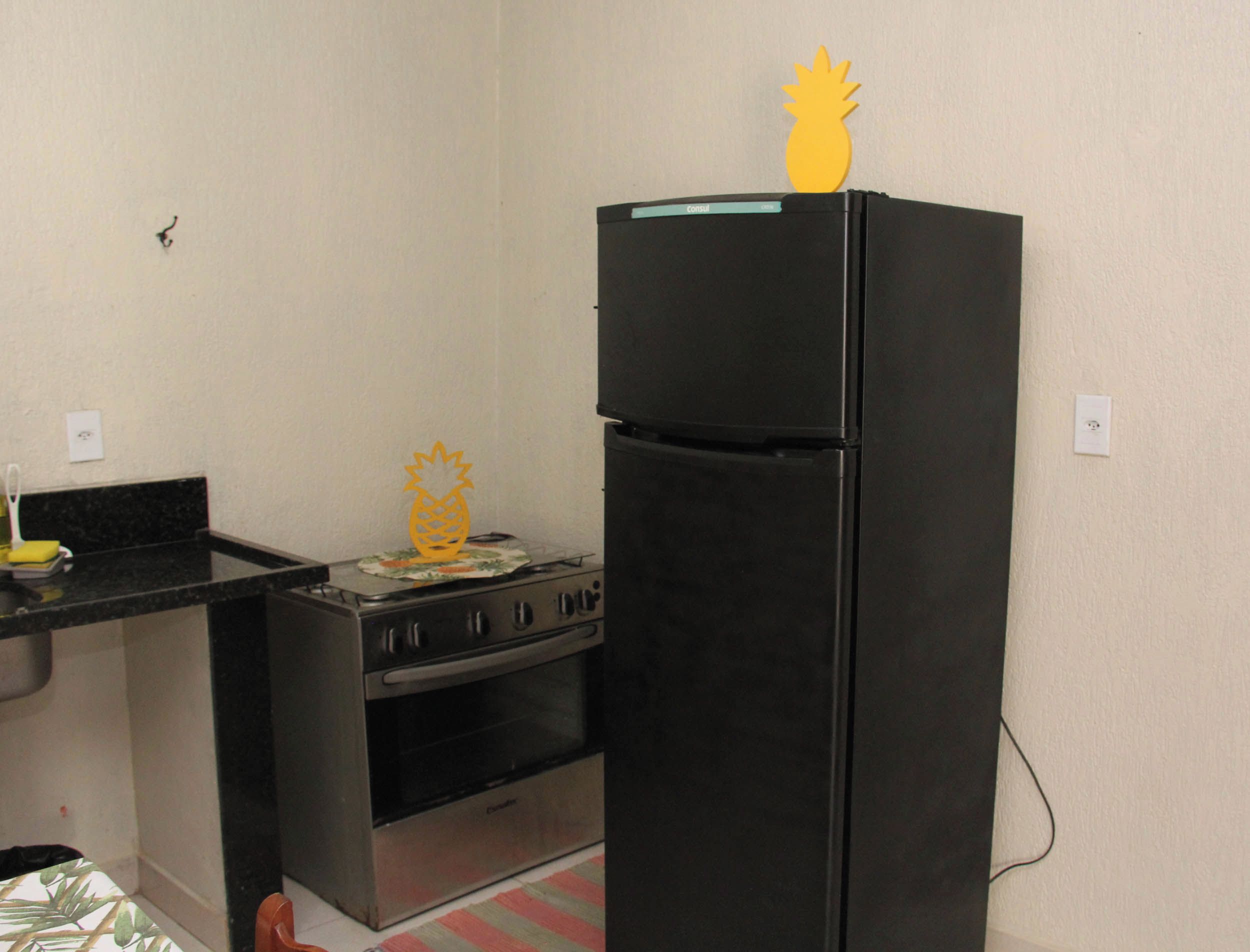 Cozinha compacta com geladeira preta, fogão e bancada pequena.