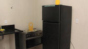 Cozinha compacta com geladeira preta, fogão e bancada pequena.