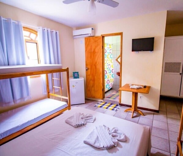 A hotel room with bunk beds, a desk, a television, and an air conditioning unit.