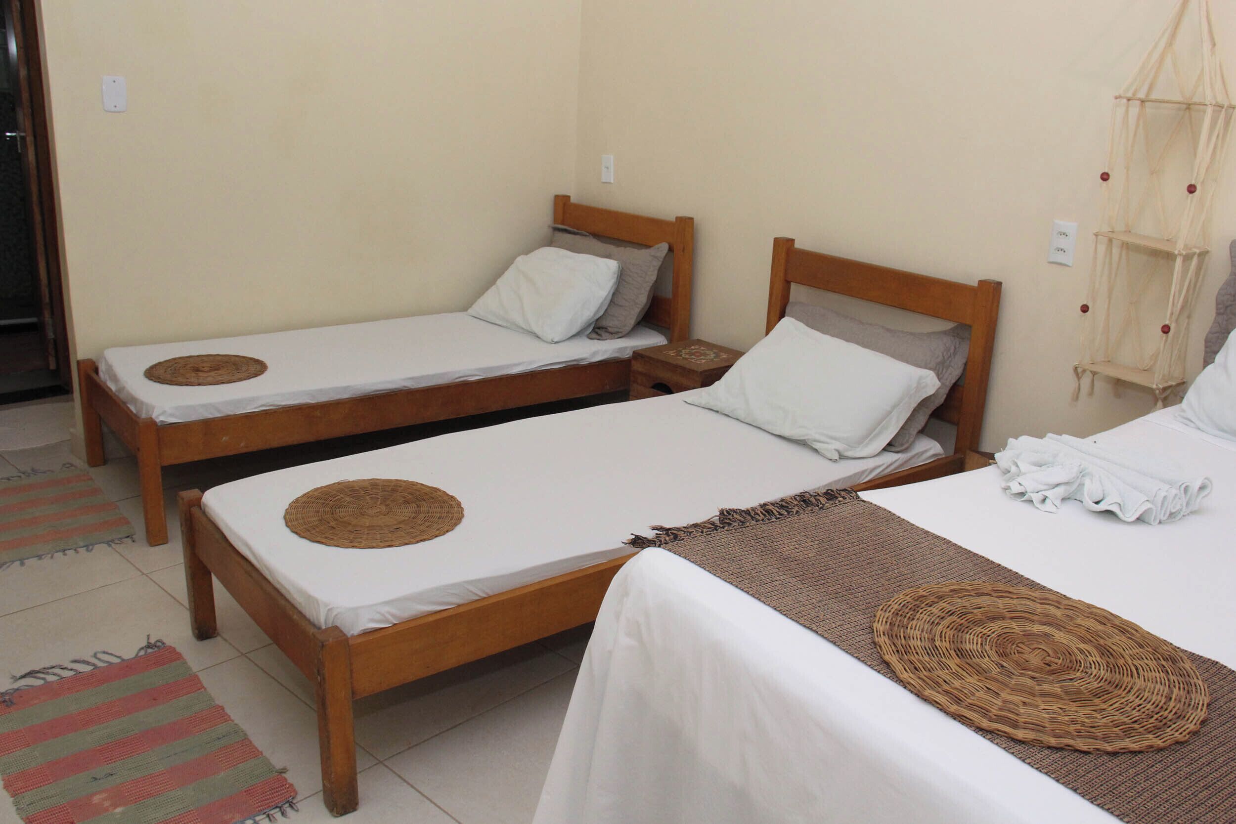 Two wooden beds with white linens and woven placemats, a hanging shelf with red accents, and a striped rug on the floor.
