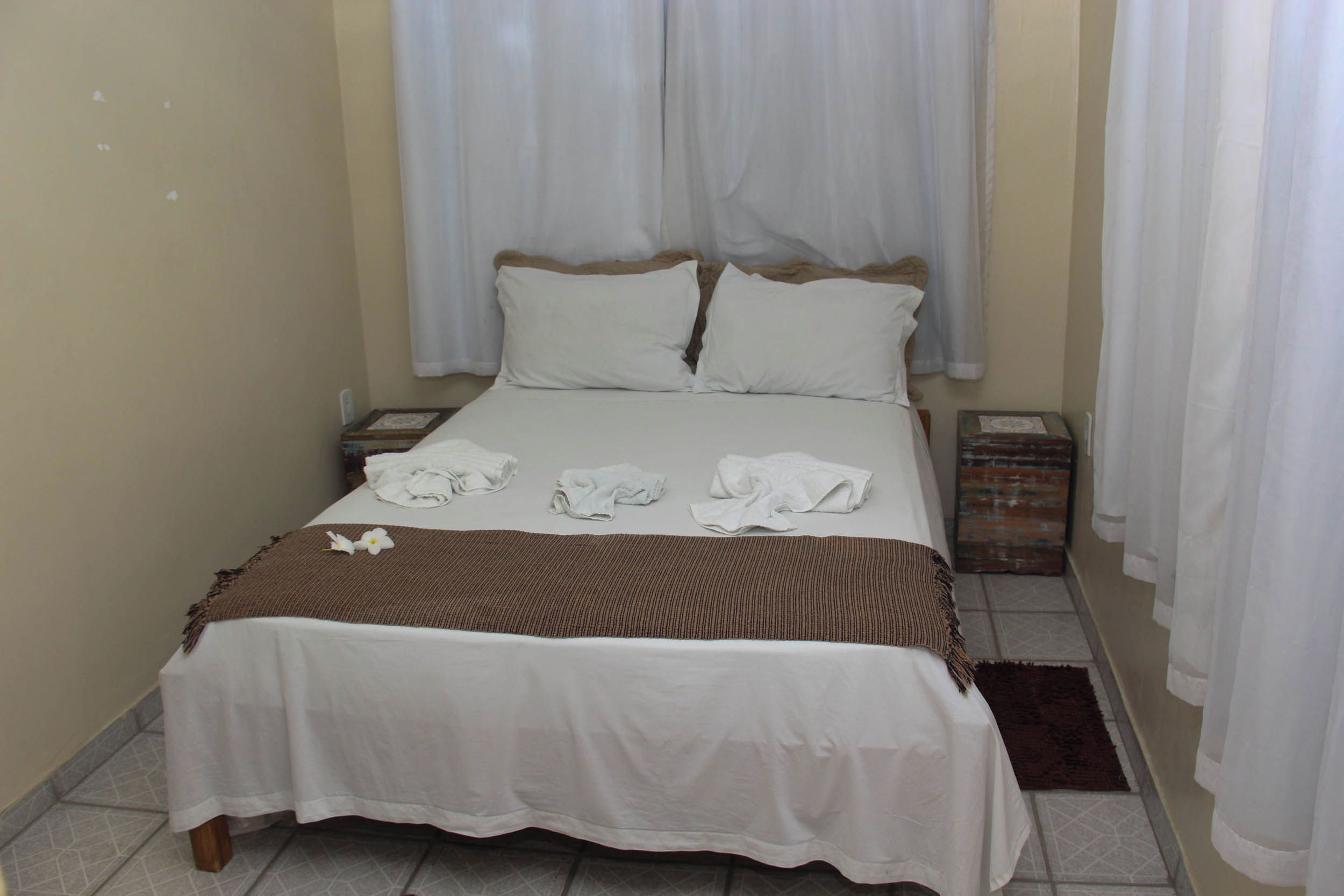 A neatly made bed with white linens and a brown throw blanket, two pillows, and a small decorative item on the bed.