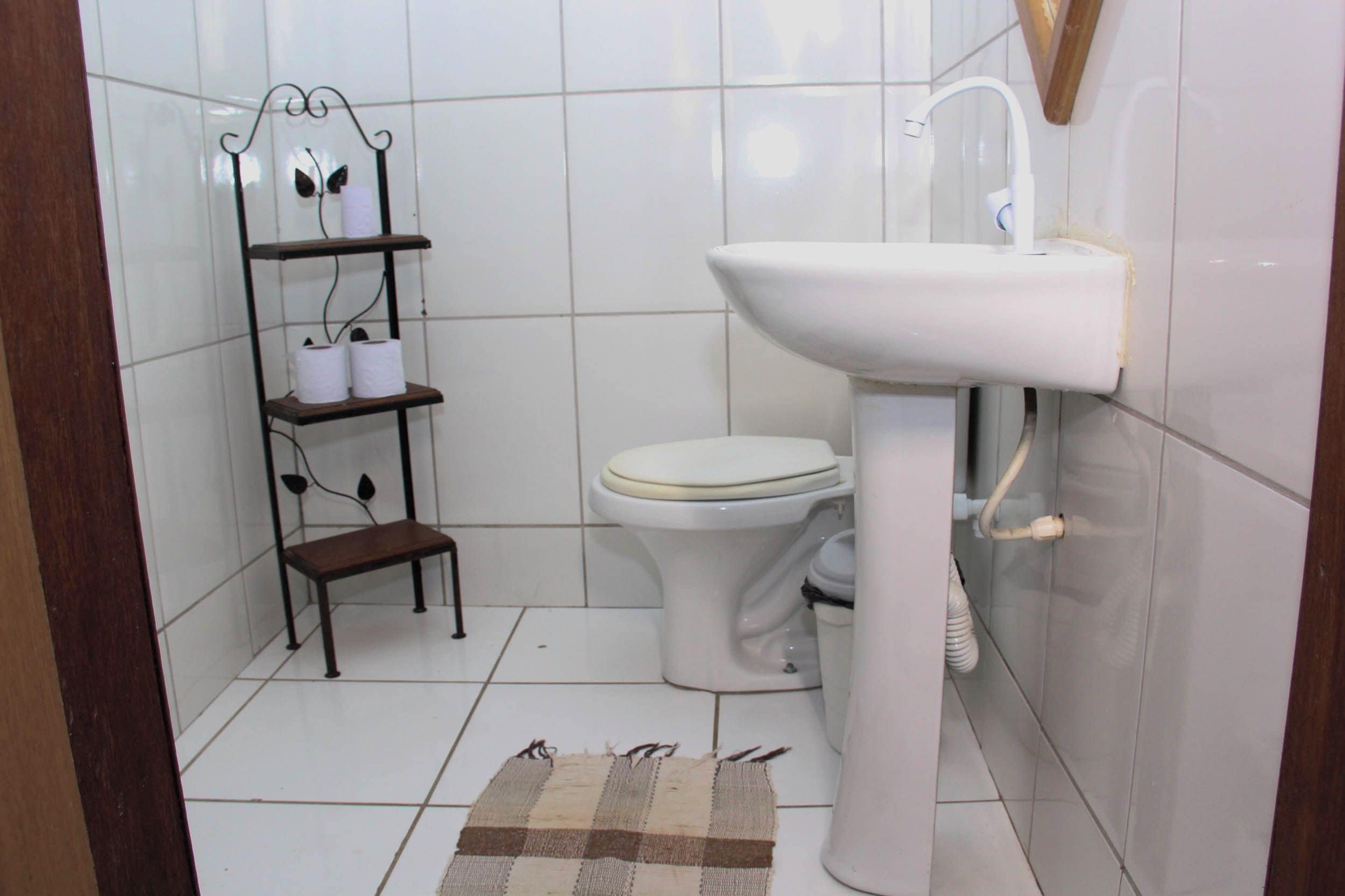 Ein Badezimmer mit Toilette, einem weißen Waschbecken, einem Ablagefach mit Toilettenpapier und einem karierten Teppich.