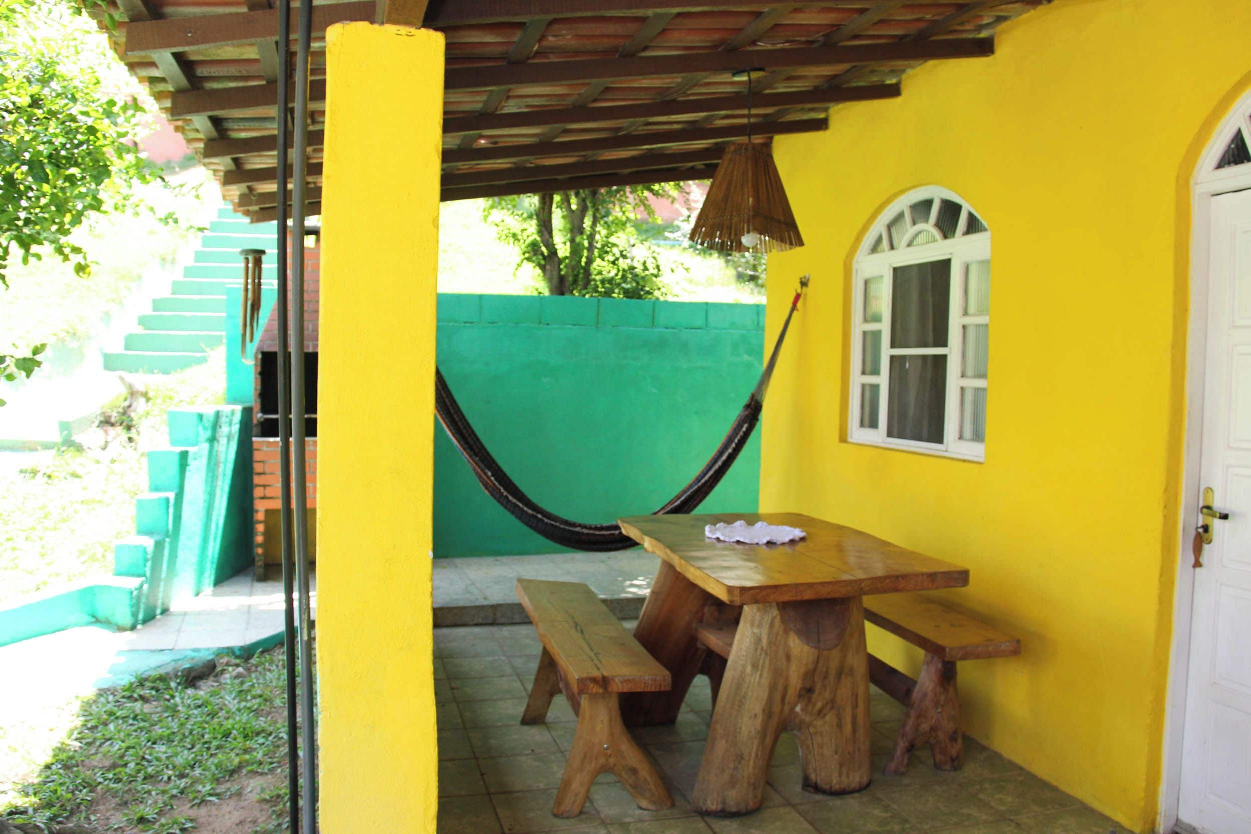 Une pièce jaune avec une table et des bancs en bois, un hamac et une fenêtre.